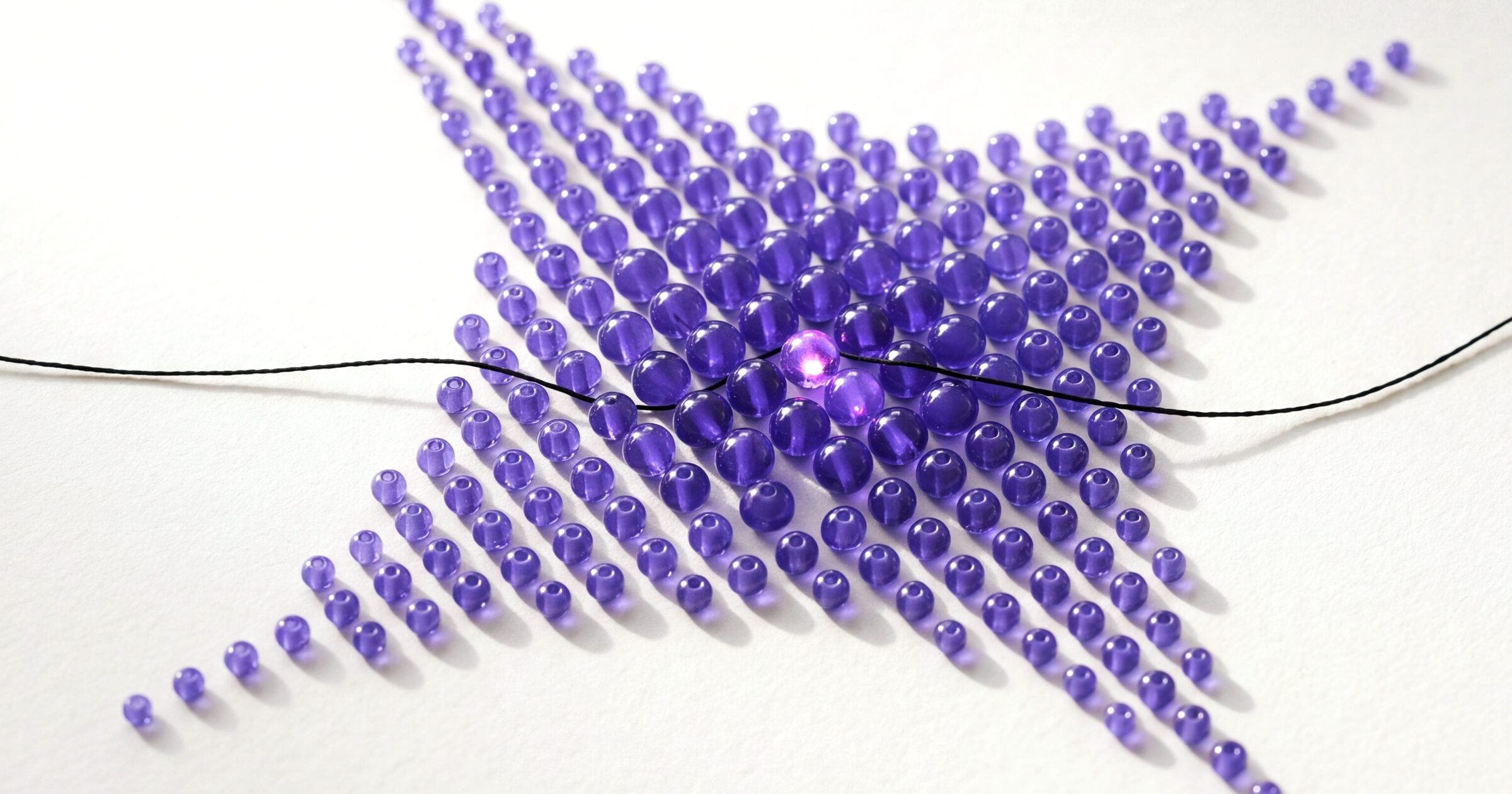The GoodCloud mark built from purple glass beads on paper, a black thread running through it.